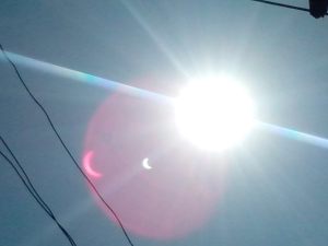 The bright light is the actual eclipse. While the little banana shaped thing in the sky is the eclipse as decoded from the camera. The sun is actually the light there, while the moon (the dark part) blocks out the light a little and gives the banana shape.